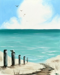 A peaceful beach scene with a sandy path leading to turquoise ocean water, lined with weathered wooden posts and a perched seagull, beneath a bright blue sky with soft clouds and distant birds in flight.