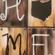 A rustic-style painting that spells out the word “HOME” using bold lettering and the shape of Ohio as the letter "O," set against a wood-textured background in warm brown tones.