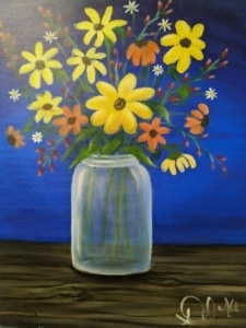 Colorful wildflowers in a glass mason jar on a wooden table with a blue background