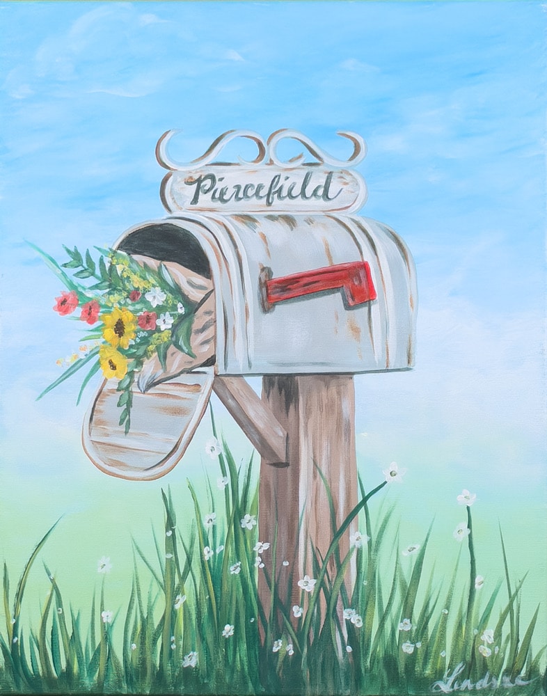 Vintage white mailbox overflowing with colorful wildflowers, standing in tall grass beneath a soft blue spring sky.